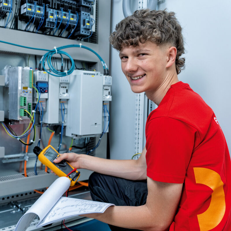 Ein Elektrotechnik-Lehrling überprüft die Verdrahtung und Funktion elektrischer Steuerungskomponenten in einem Schaltschrank.